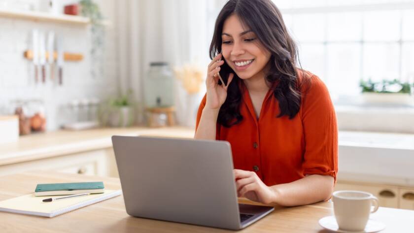 Focused woman on phone with laptop at home